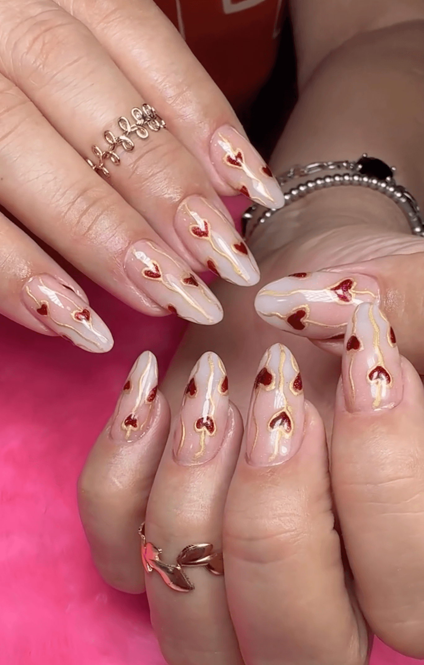 Uñas nude con corazones rojos y foil dorado en diseño artístico