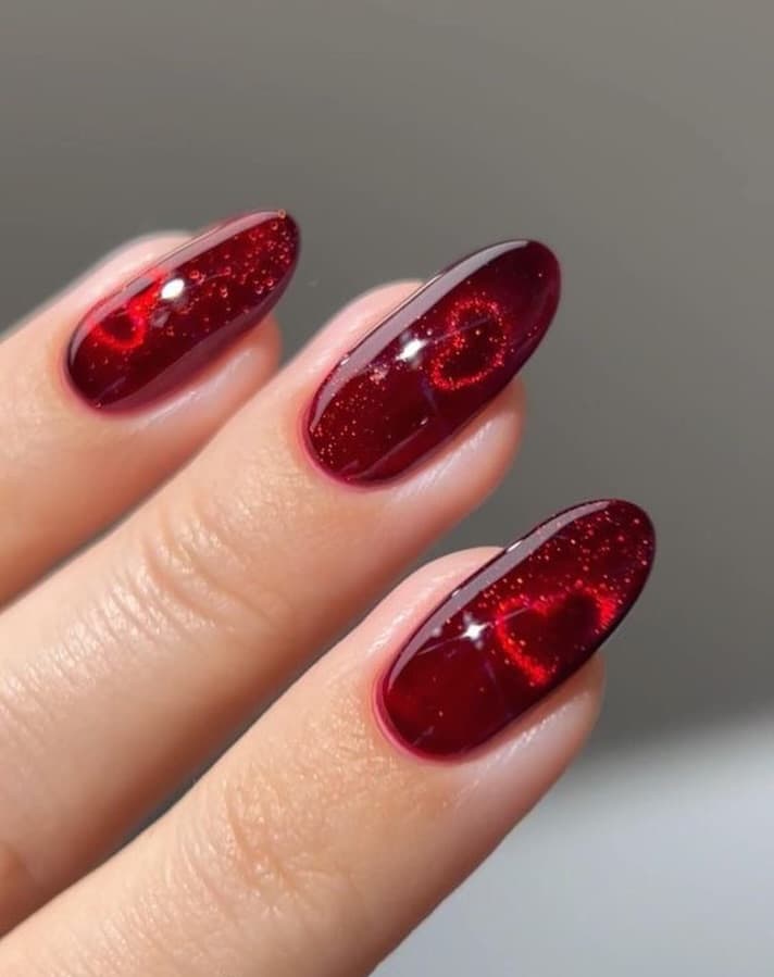Short dark red nails with cat-eye finish and heart detail on each nail